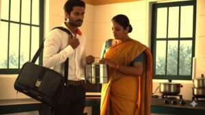"Indian wife handing lunchbox to husband leaving for office in the morning kitchen scene."